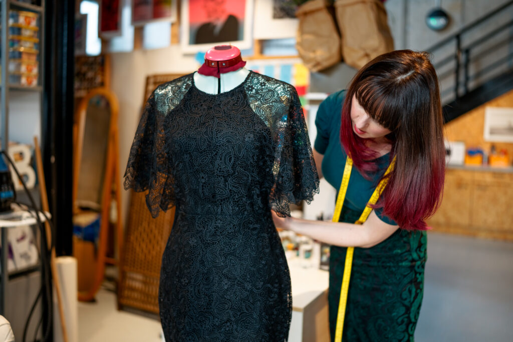 Tailor adjusting a black lace dress on a mannequin in an ethical London studio.