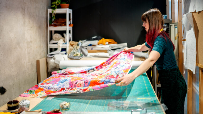 Person folding vibrant patterned fabric in a sewing studio with cutting mat and fabric rolls