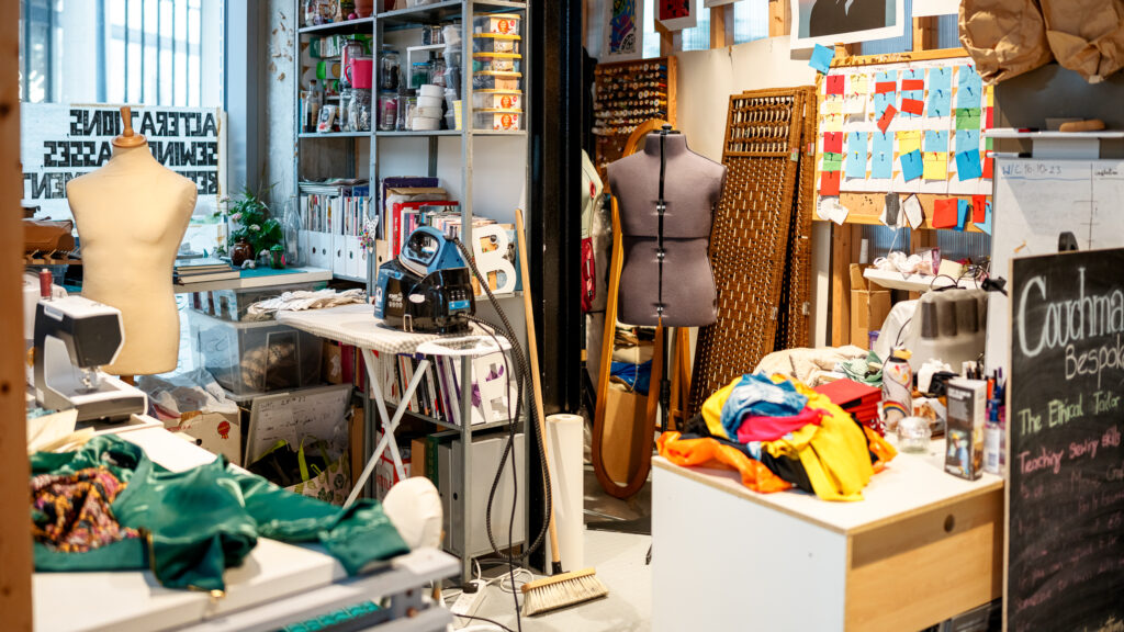 A working tailoring studio at Couchman:bespoke with sewing machines, fabric rolls, and materials ready for repair.